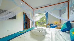 A room with a bed, a small table, and a chair. There is a window with curtains and a view of greenery outside. - Sea Village Homestay (Da Nang)