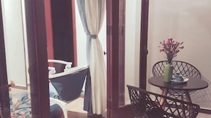 A room with a dining area featuring a round table and chairs, a small potted plant, and a view through an open door leading to a balcony with a chair and a table. - Sea Village Homestay (Da Nang)