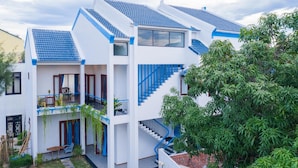 A multi-story building with a white exterior and blue accents, featuring balconies, a staircase, and a garden area. - Sea Village Homestay (Da Nang)