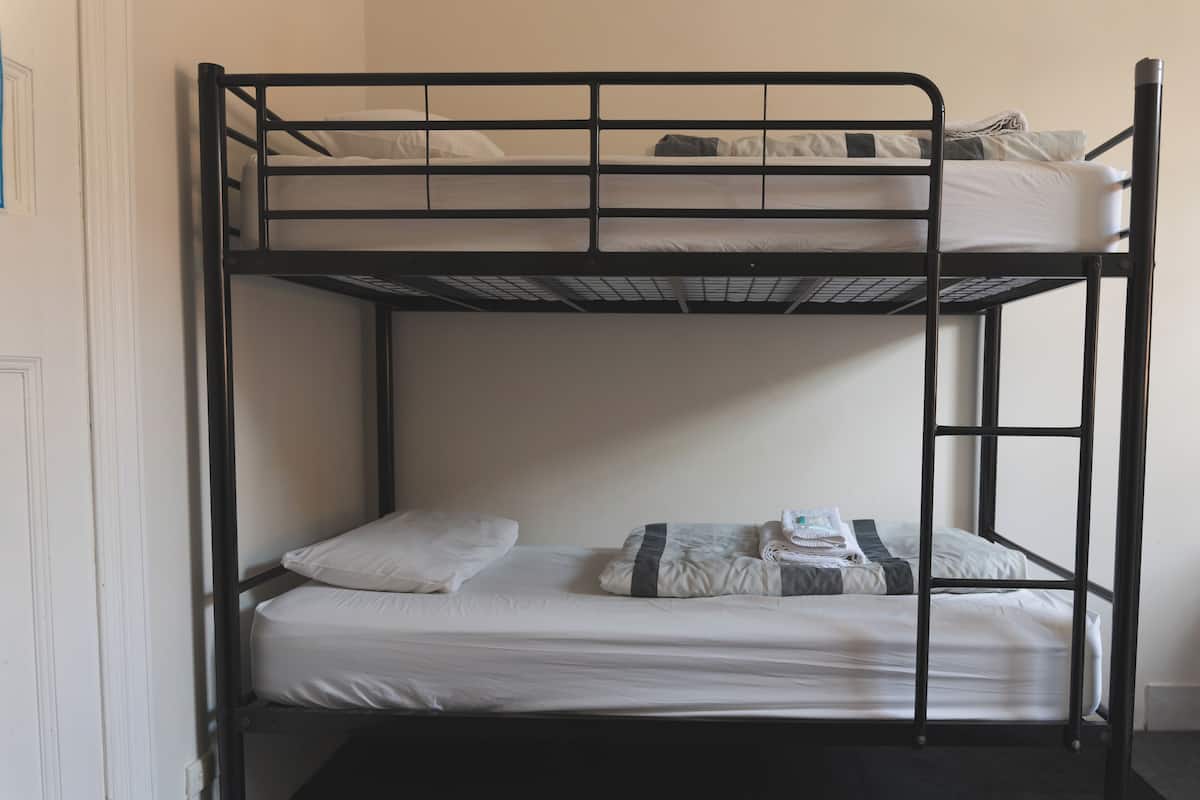 Una cama litera con dos niveles, ropa de cama blanca y suelo gris.