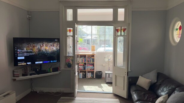 A living room with a television, a bookshelf, a leather couch, and a door leading to another room. - Manly Bunkhouse - Hostel (Manly)