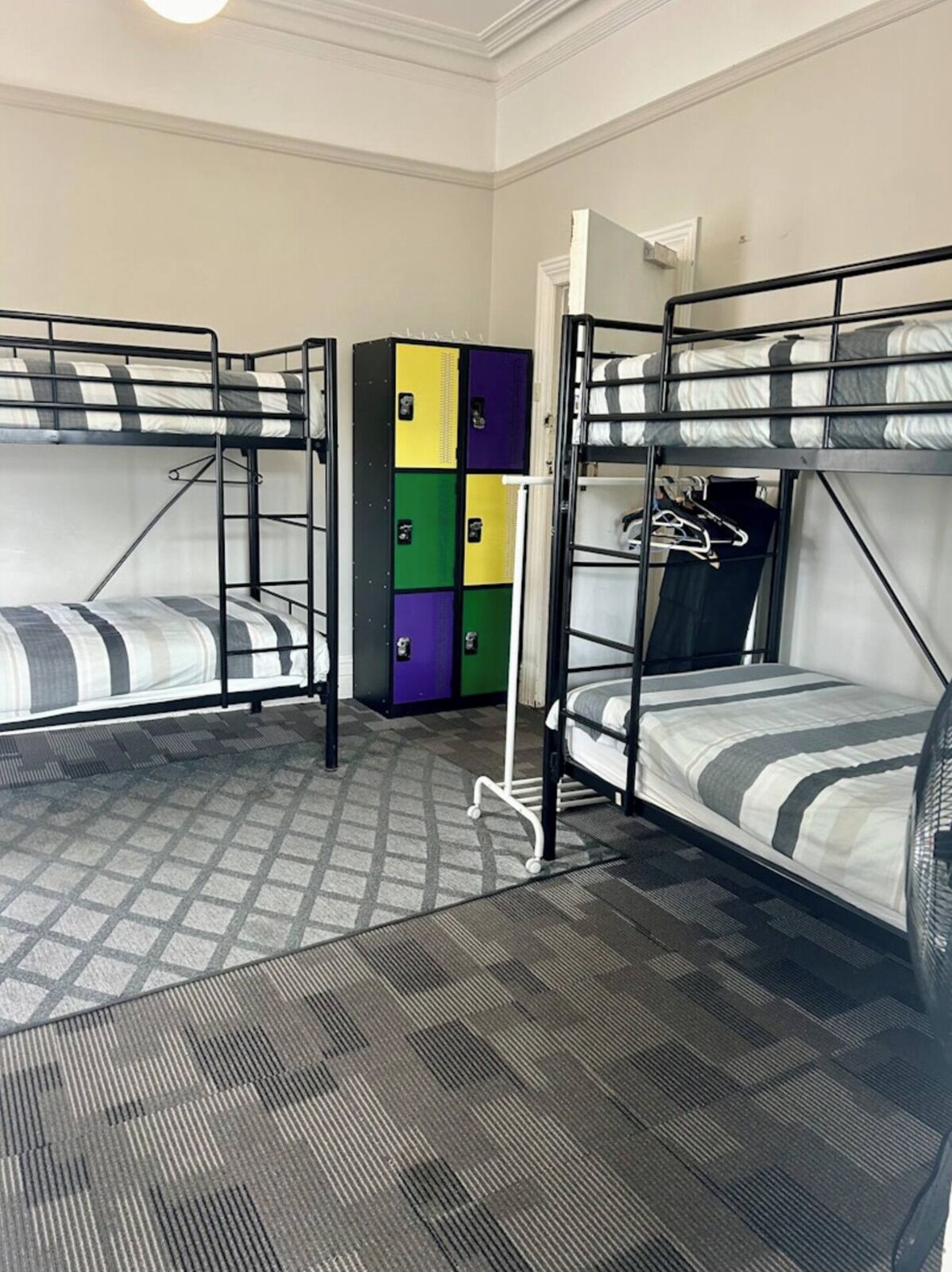 A dormitory room with bunk beds, a storage unit with colorful lockers, and a patterned carpet.