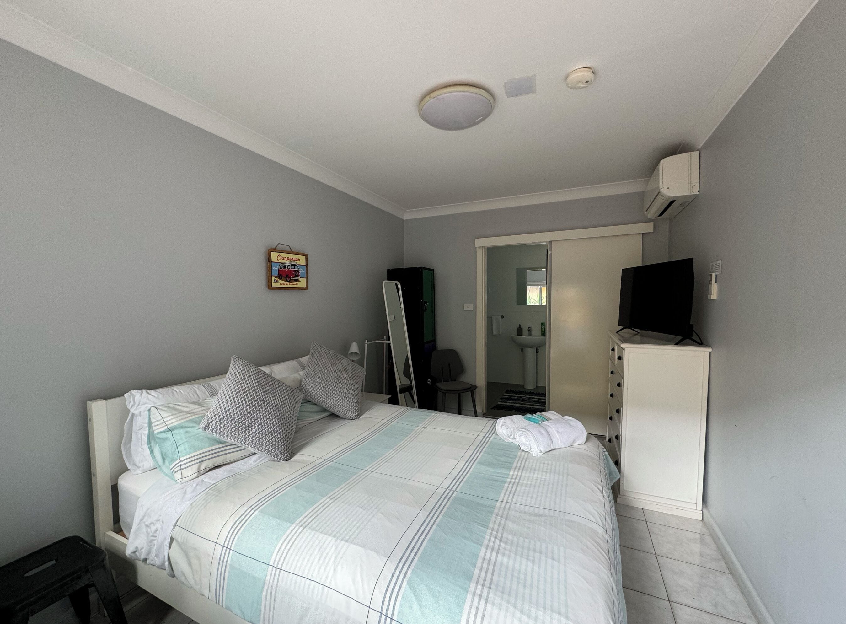 A bedroom with a bed, a dresser, a television, and a bathroom visible through an open door.