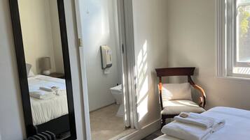 Una habitación de hotel con cama, una silla, inodoro y espejo.