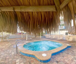 Uma piscina com cobertura de palha, rodeada por espreguiçadeiras e um deck pavimentado.