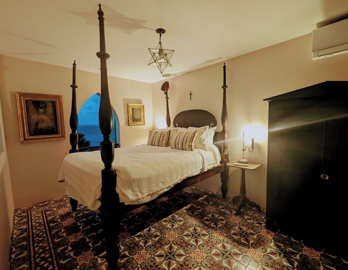 A four-poster bed with a star-shaped ceiling light, a bedside table with a lamp, and a patterned floor.