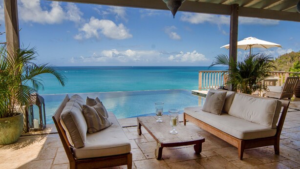A covered outdoor seating area with a view of the ocean, a pool, and a patio with a table and chairs. - 5 bedroom villa with pool in stunning clifftop location next to gorgeous beach (Rogues Bay)
