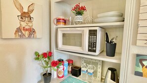 Una cocina con microondas, cafetera, taza y planta en maceta.