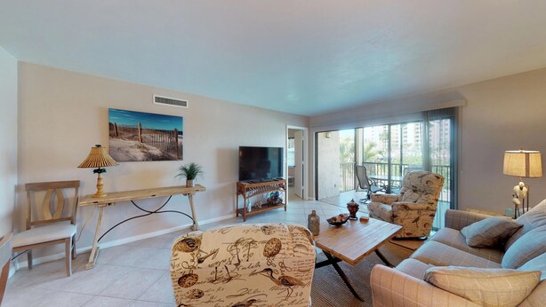 A living room with a sofa, armchair, TV, and a painting on the wall. - Desirable Location, Directly Across Street From South Beach Access!!! (Marco Island)
