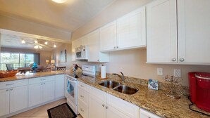 A modern kitchen with white cabinets, granite countertops, a double sink, and a red coffee maker. - Desirable Location, Directly Across Street From South Beach Access!!! (Marco Island)