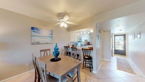 A dining area with a wooden table and chairs, a ceiling fan, and a kitchen in the background. - Desirable Location, Directly Across Street From South Beach Access!!! (Marco Island)