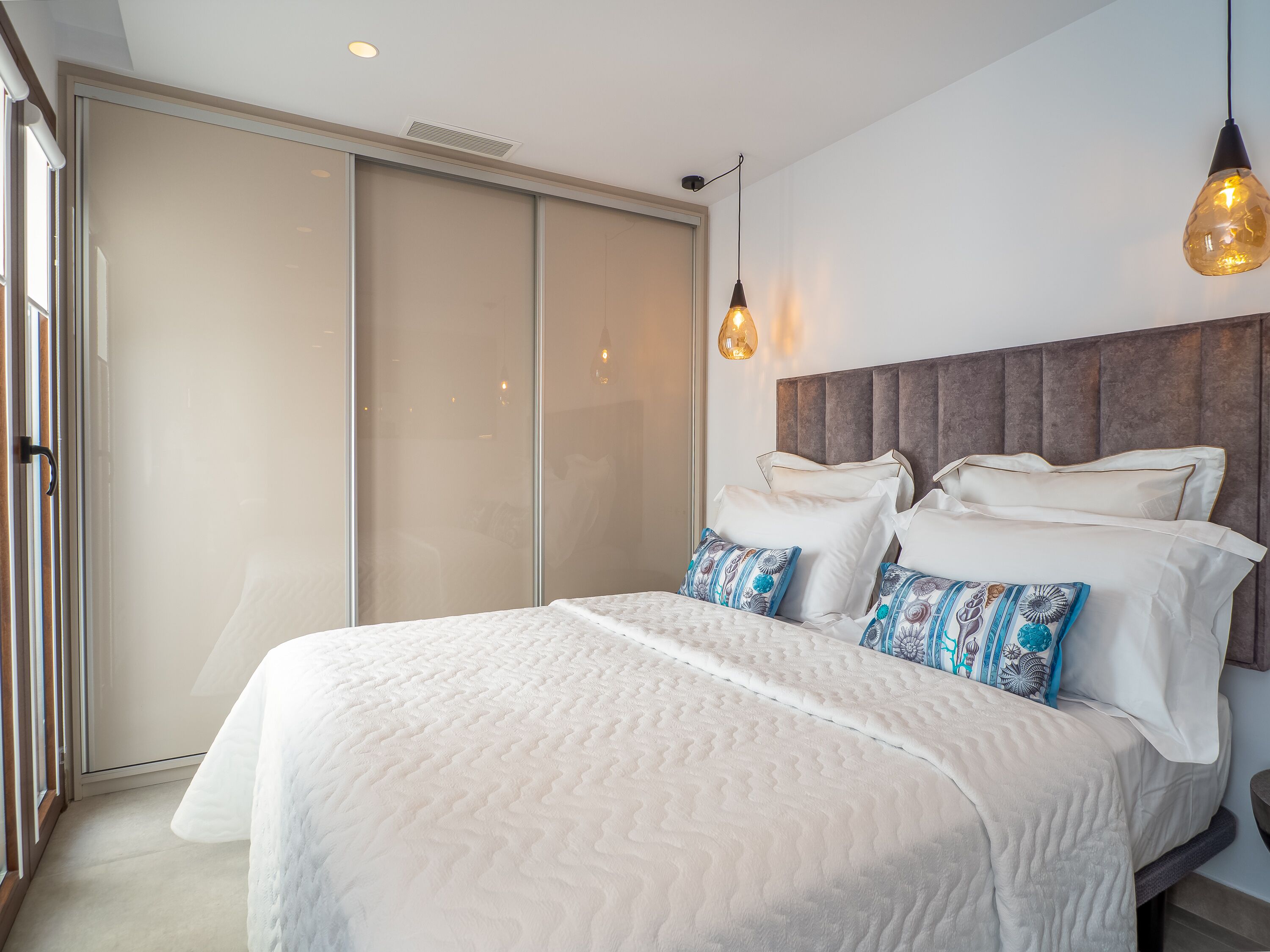 Un dormitorio con una cama grande, un ventanal corredero y una lámpara colgante.