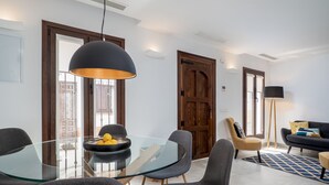 Een moderne eetruimte met een glazen tafel, grijze stoelen en een zwarte hanglamp.