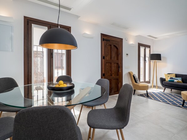 Un comedor moderno con una mesa de vidrio, sillas grises y una lámpara colgante negra.