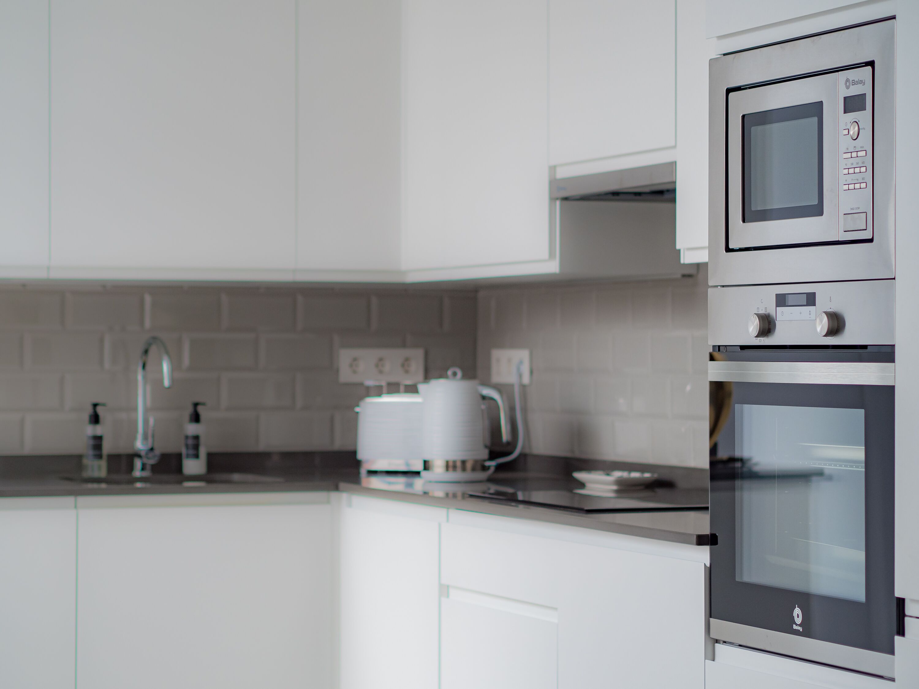 Una cocina moderna con armarios blancos, una campana extractora de acero inoxidable y un horno empotrado.