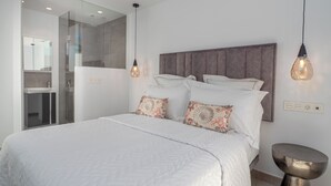 Een moderne slaapkamer met een groot bed, een douchecabine van glas en een hanglamp.