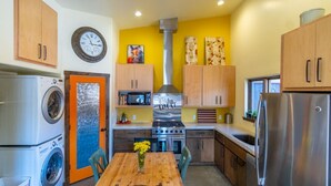 A compact kitchen with a central stove, a washing machine, a microwave, and a refrigerator.