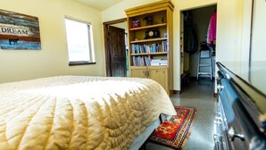 A bedroom with a large bed, a bookshelf, a ladder, and a door leading to another room.