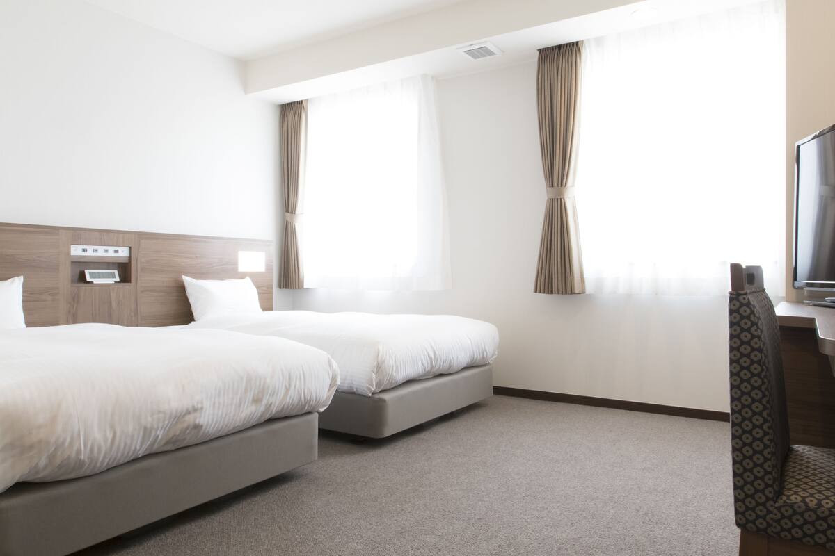 A hotel room with two beds, a TV, and a desk.