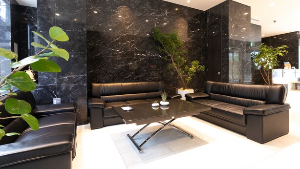 Uma sala de estar moderna com sofás de couro preto, uma mesa de centro de vidro e uma grande parede de mármore preto.