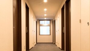 Corredor de hotel com portas em ambos os lados, uma janela no fim e piso coberto de carpete.