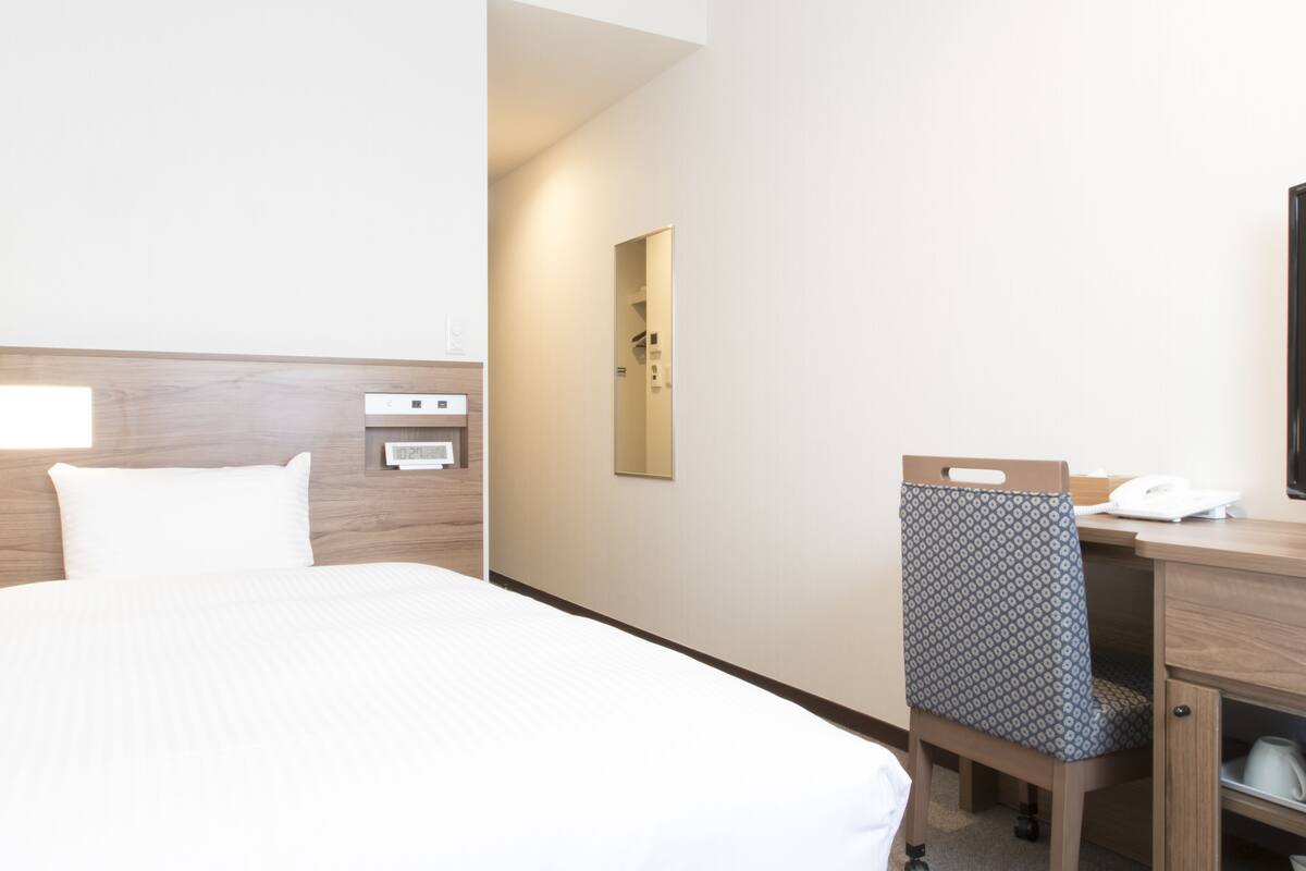 A hotel room with a bed, bedside table, chair, desk, and a mirror.