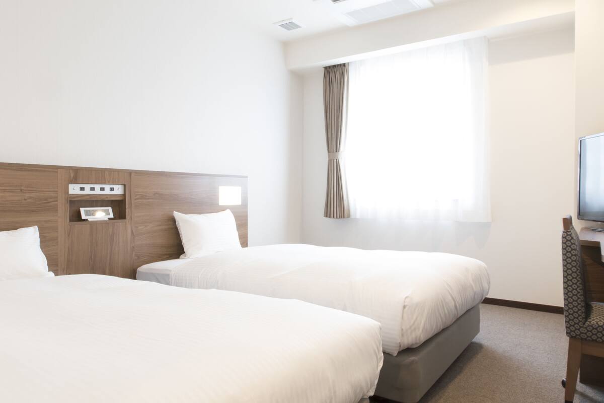 A hotel room with two beds, a TV, and a window with curtains.