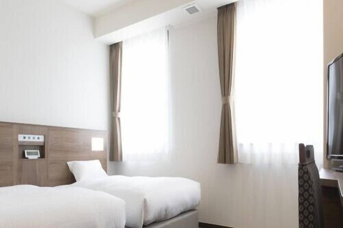 A hotel room with two beds, a TV, and a window with curtains.