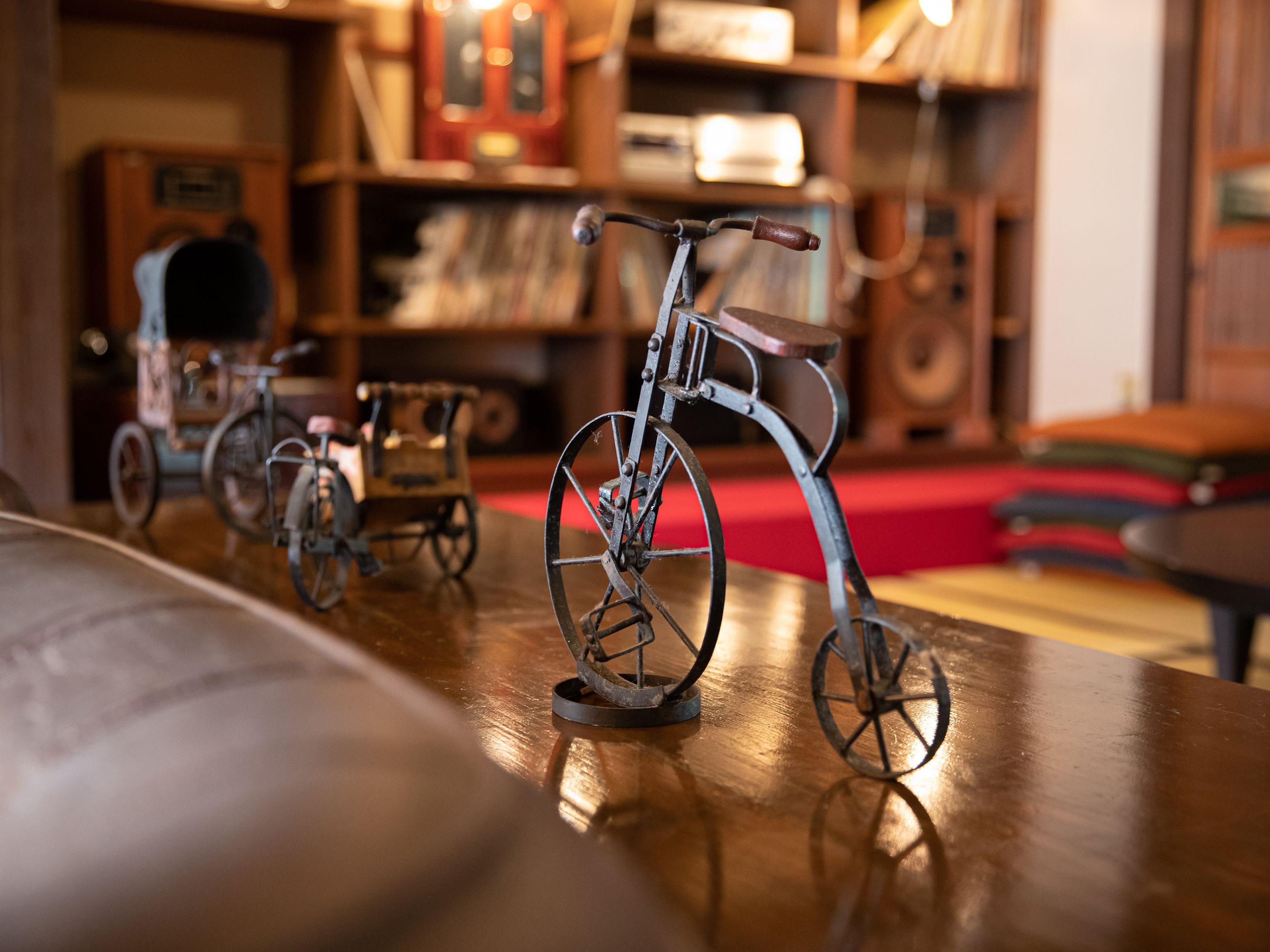 A vintage bicycle on a wooden table in a room with a red carpet and wooden shelves in the background.