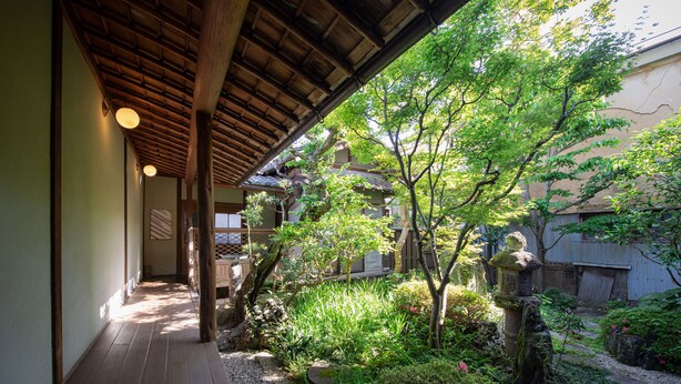 A traditional Japanese garden with a wooden walkway, stone path, and various plants.
