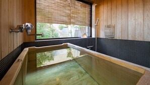 A wooden interior with a glass-enclosed hot tub, wooden walls, and a window with blinds.