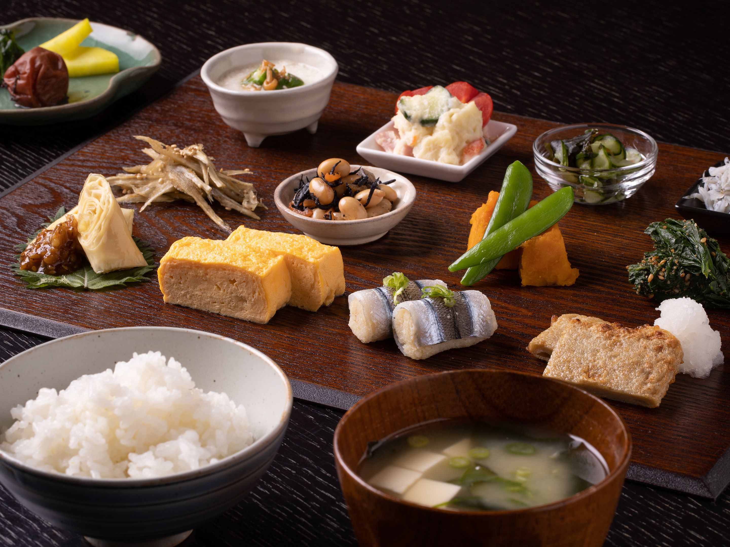 A variety of Japanese dishes including rice, tofu, fish, and vegetables on a wooden table.