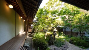 A traditional Japanese garden with a wooden walkway, stone lanterns, and lush greenery.
