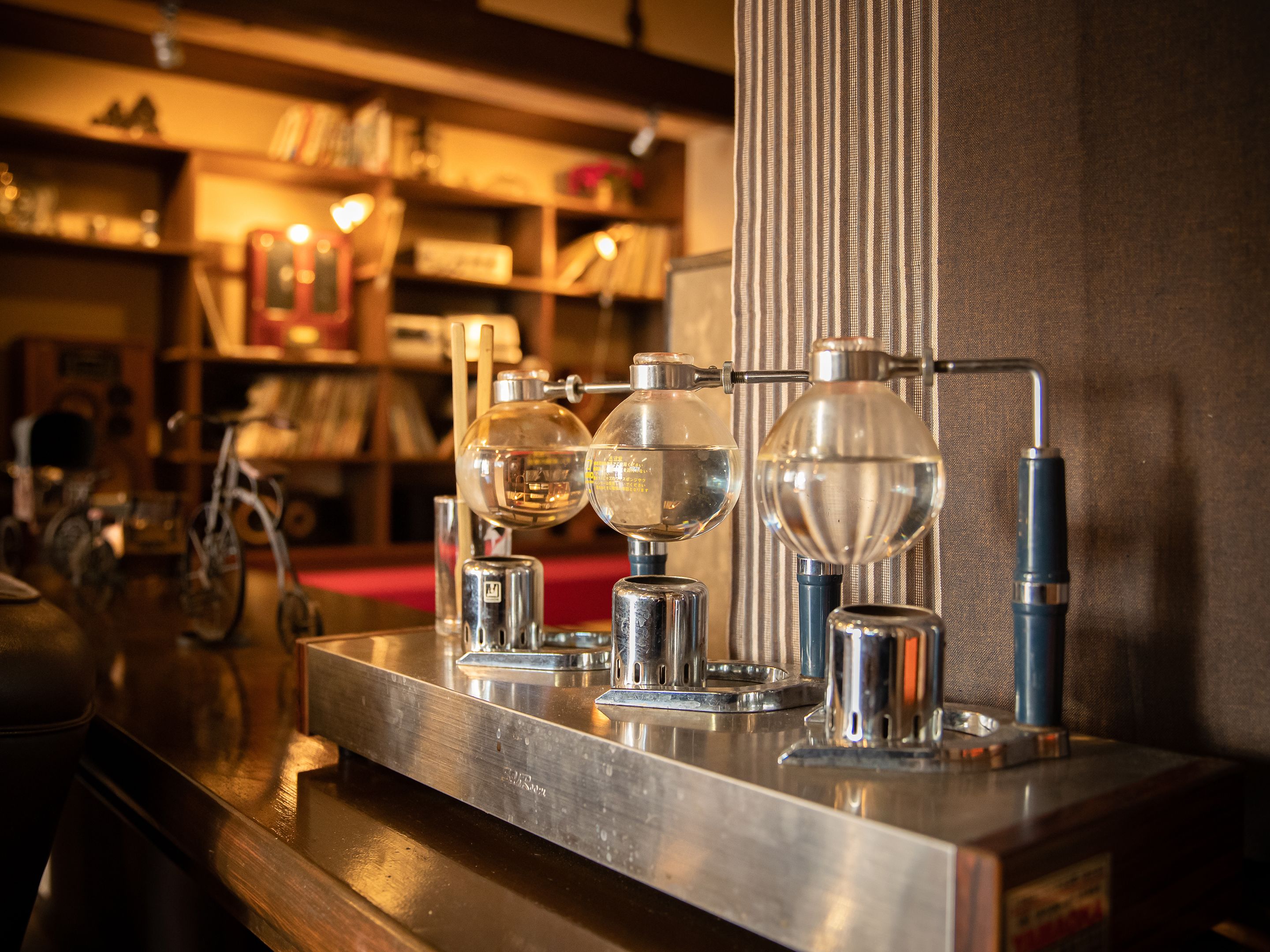 A bar area with a polished metal counter, a glass display case, and a bicycle in the background.
