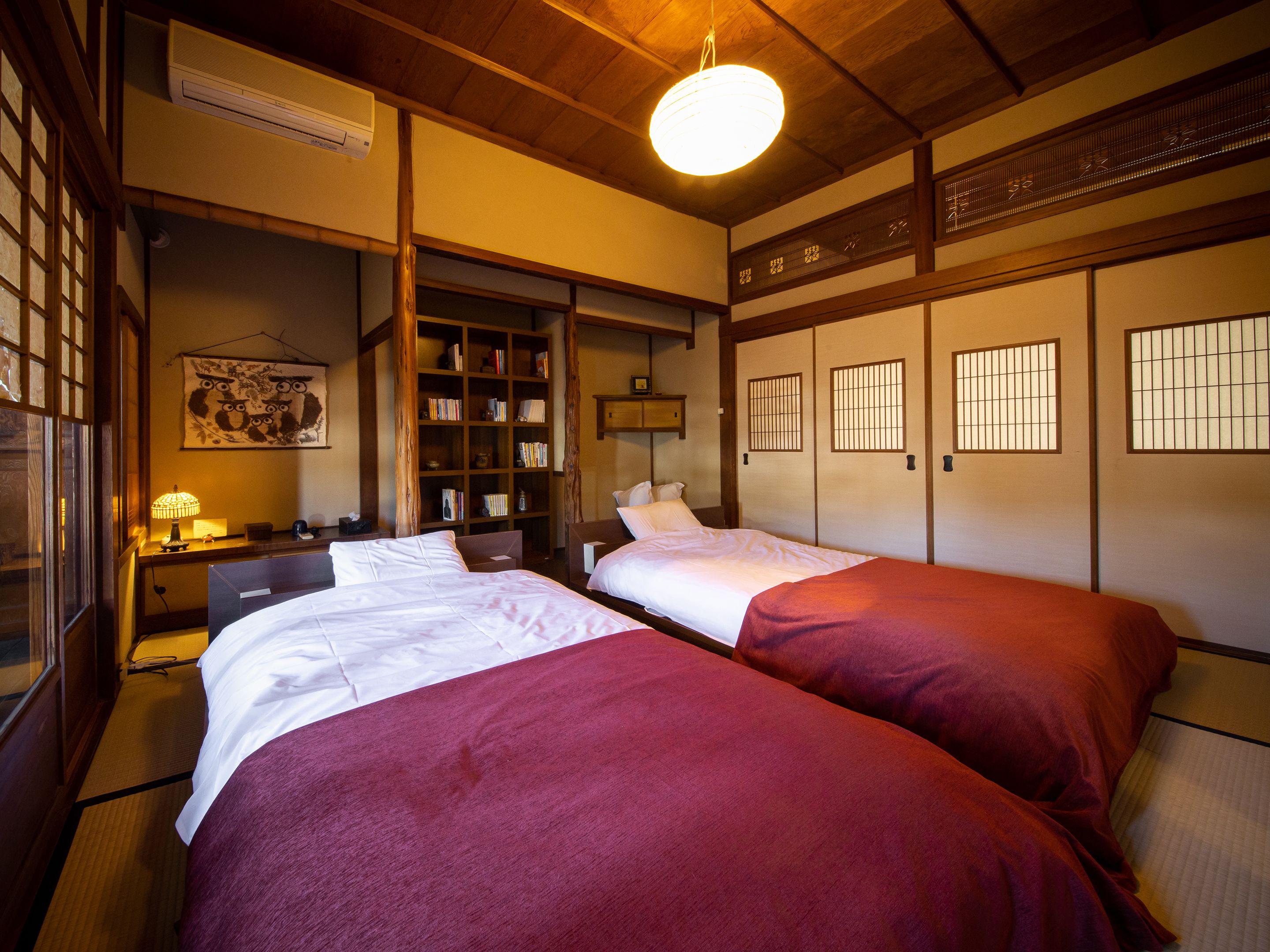 Une pièce de style japonais traditionnel, comprenant deux lits, une bibliothèque et une lampe suspendue.