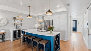 Een moderne keuken met een centraal eiland, barstoelen, hanglampen en roestvrijstalen apparatuur.