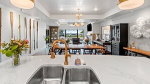 Een moderne keuken met een groot eiland, een roestvrijstalen spoelbak en een gouden kraan. Op het eiland staat een vaas met bloemen en aan de muur hangt een collectie houten vleermuizen.