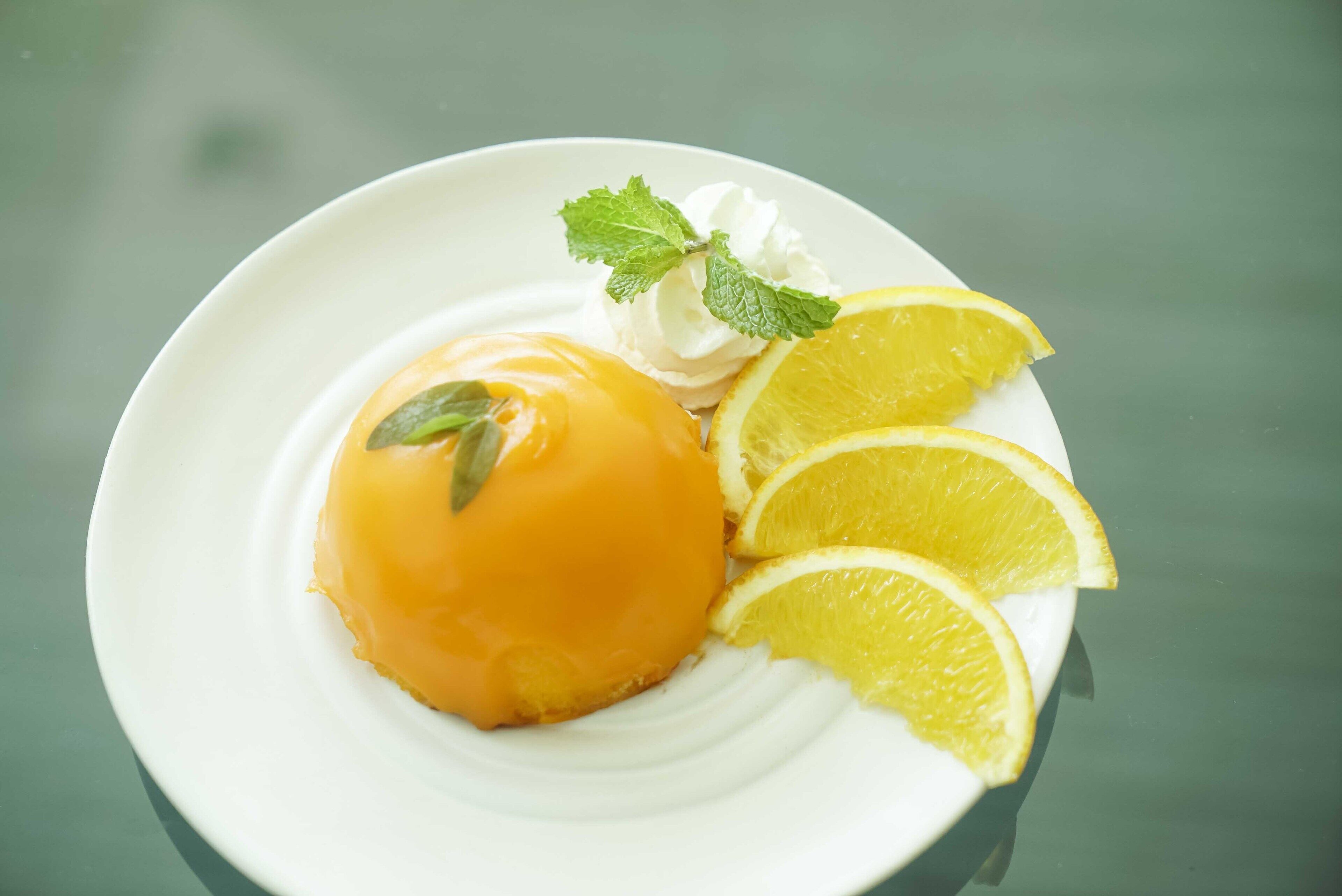 A dessert with a creamy topping, lemon slices, and mint leaves on a white plate.