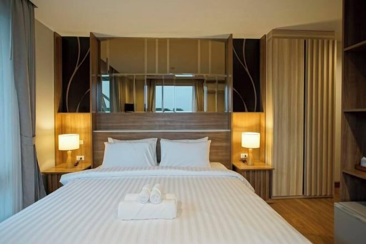 A hotel room with a large bed, two bedside tables with lamps, a mirror above the bed, and a view of the city through the window.