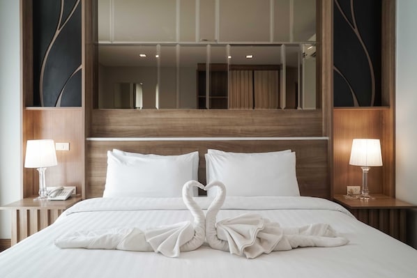 A hotel room with a large bed, two bedside lamps, a mirror above the bed, and a wooden headboard.