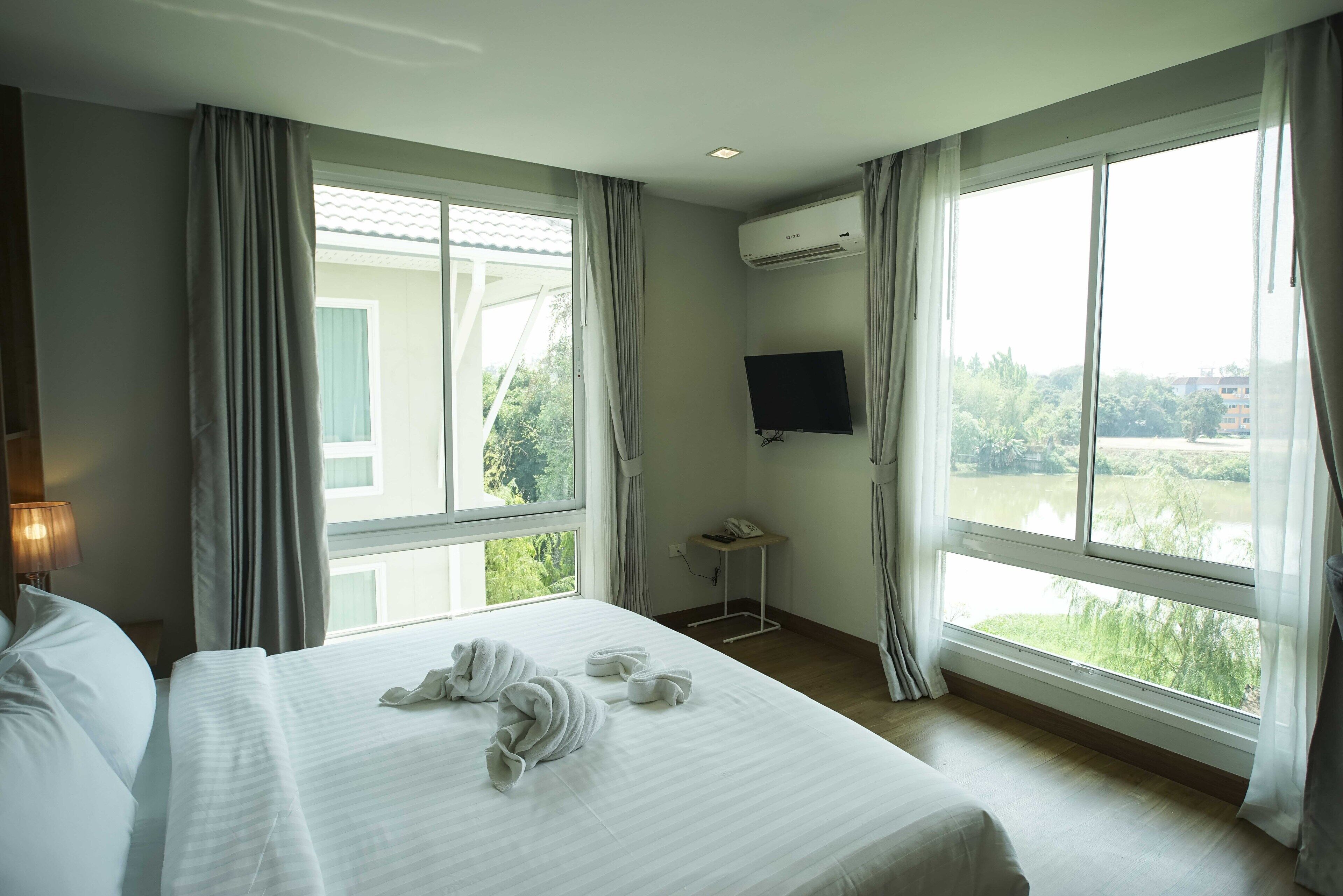 A hotel room with a large bed, a TV mounted on the wall, and a window with curtains.