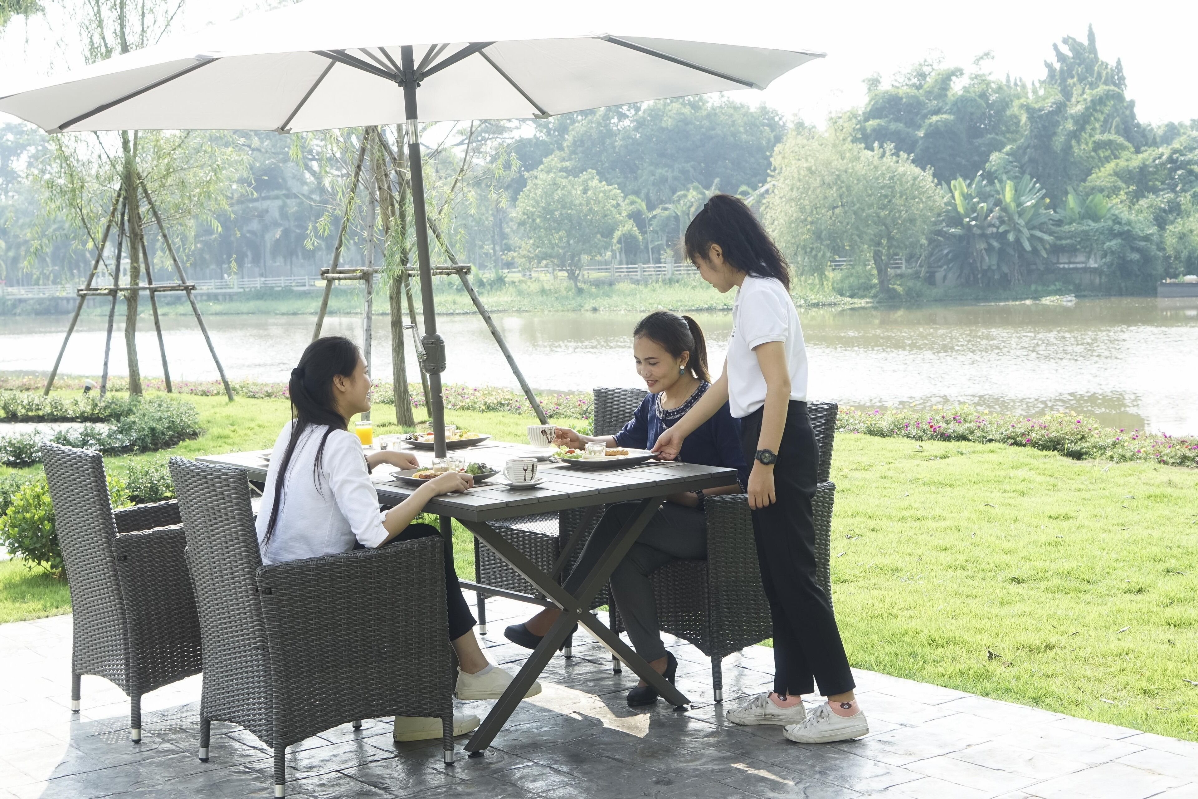 Un área de comedor con sillas de mimbre y una mesa, rodeada por un jardín exuberante y una extensión de agua.