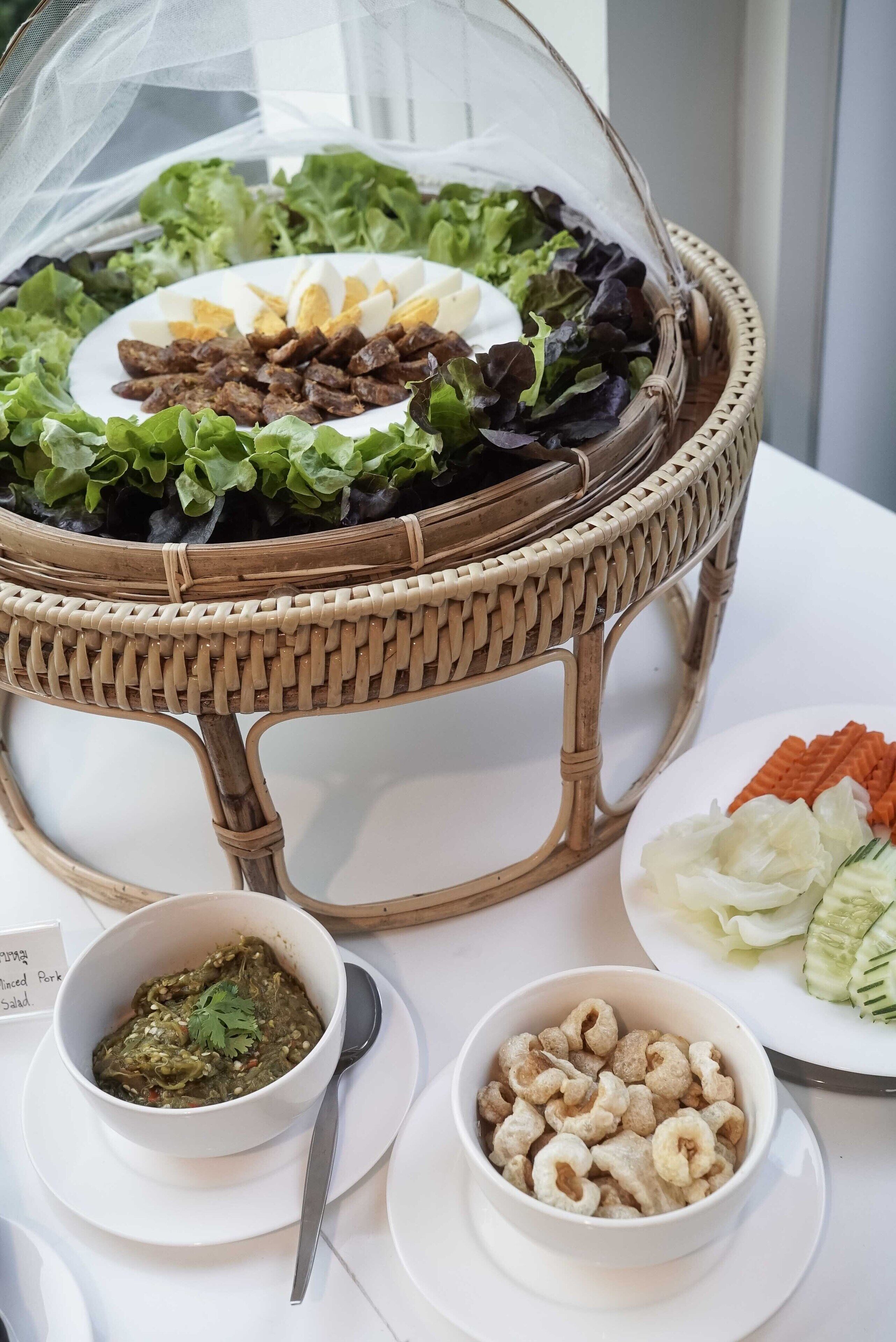 A buffet table with a variety of dishes including a salad, a bowl of soup, and a plate of vegetables.