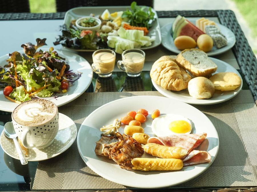 Una mesa de desayuno con platos de comida, entre ellos huevos, tocino, maíz y tostadas, además de una taza de café y una ensalada.