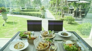 A dining table with various dishes, wicker chairs, and a garden view. - Nantra Chiangmai Riverfront Hotel (Chiang Mai)