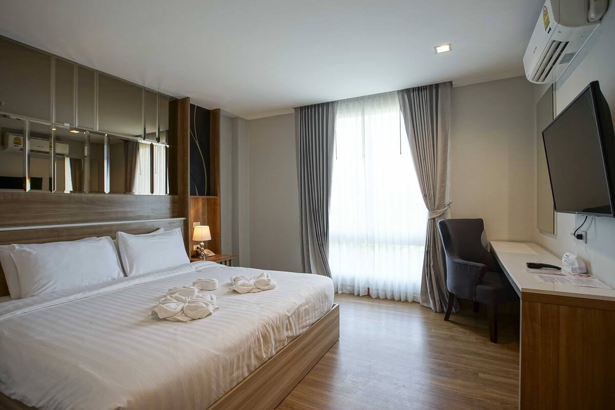 A hotel room with a large bed, a desk with a chair, a TV, and a window with curtains.
