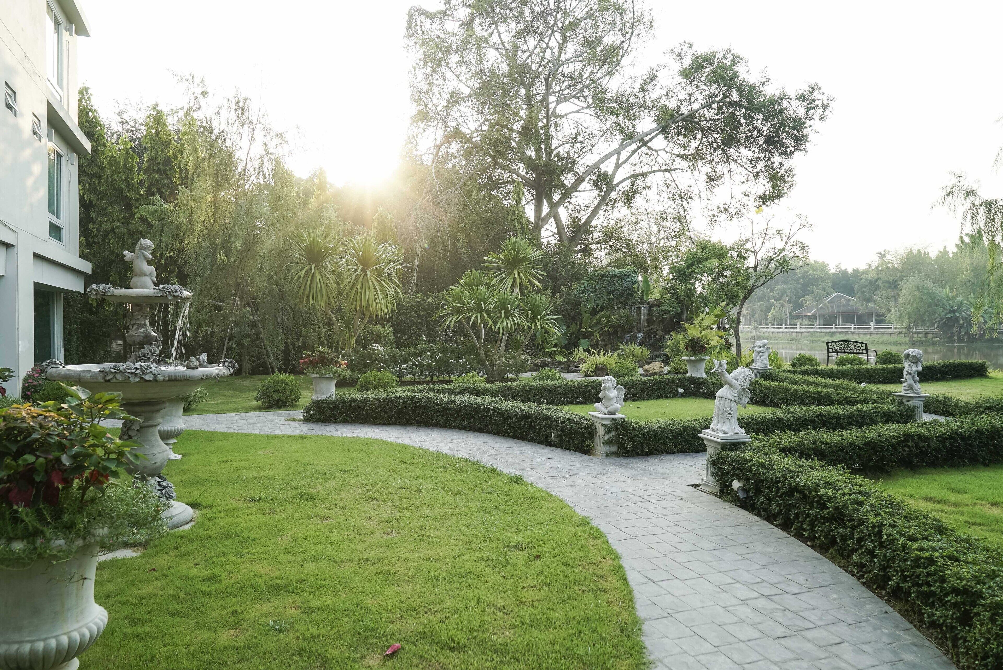 Een verzorgde tuin met een kronkelend pad, beelden en een gebouw op de achtergrond.