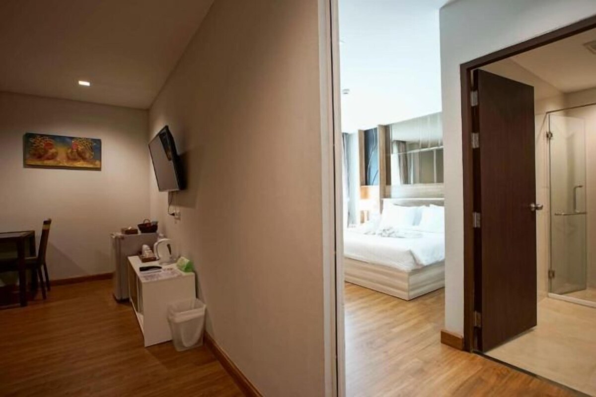 A hotel room with a bed, a desk with a chair, a television, and a small trash bin.
