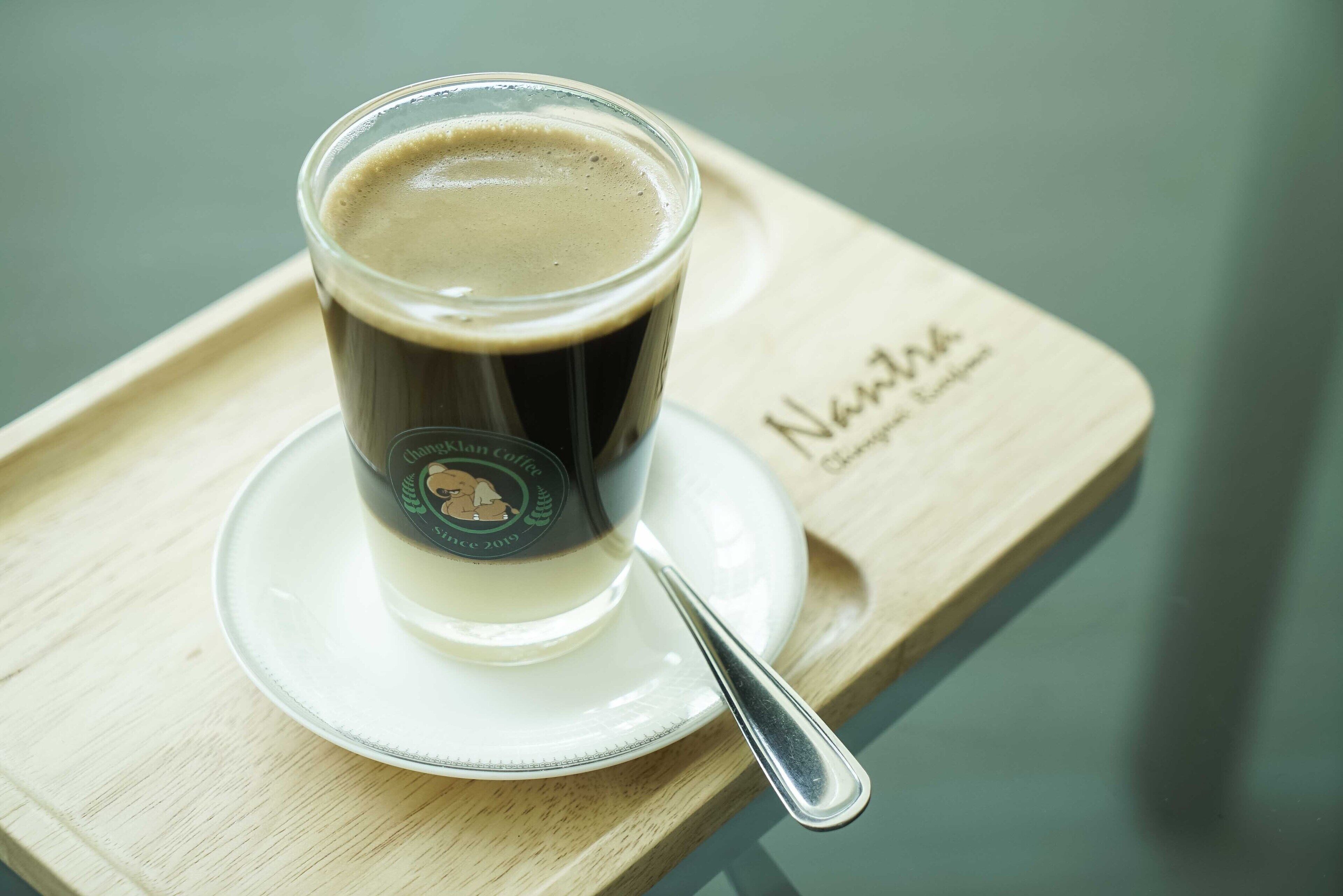 Eine Kaffeetasse auf einem Tablett mit einem Löffel, platziert auf einem Tisch mit Holzbeschichtung.