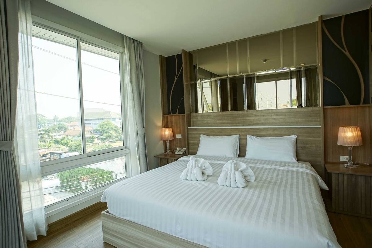 A hotel room with a large bed, two bedside lamps, a nightstand, and a view of the outside.
